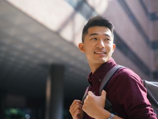 Asian man looking up and holding his backpack