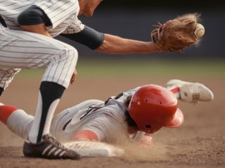 Base runner sliding into base while fielder catches a ball in baseball game