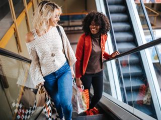 Two women looking at each other and smiling while on a scalator at a shopping center