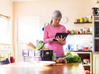 Woman at kitchen checking groceries on tablet