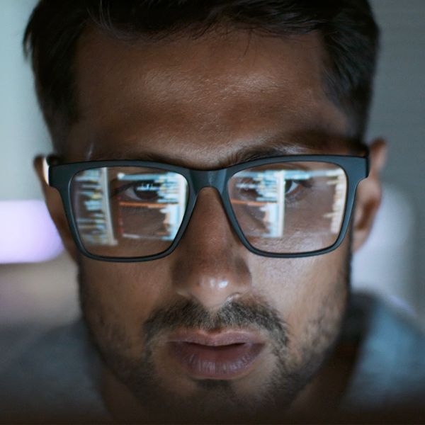 A focused man wearing glasses with computer code reflecting in the lenses.