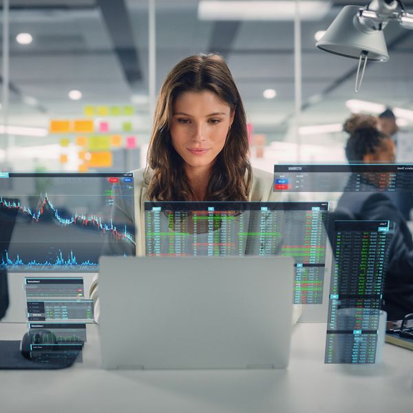 A woman working in an office surrounded by multiple digital screens displaying financial data and charts.