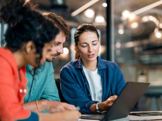 A diverse team of colleagues reviewing a project on a laptop in a modern office.