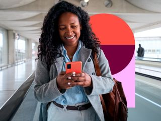 A smiling woman with curly hair looks at her smartphone while walking through a modern, bright transit terminal.