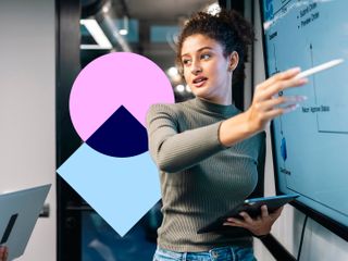 A professional woman pointing to a data flowchart on a large digital screen while holding a tablet in a modern office environment.