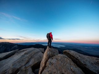 A man on the peak of a mountain overlooking the sunset