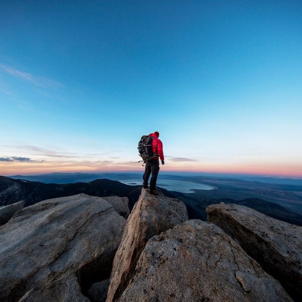 A man on the peak of a mountain overlooking the sunset