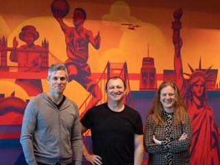 CI&T founders Bruno Guicardi and Cesar Gon with EMEA director Carolina Wosiack smiling and standing in front of a mural